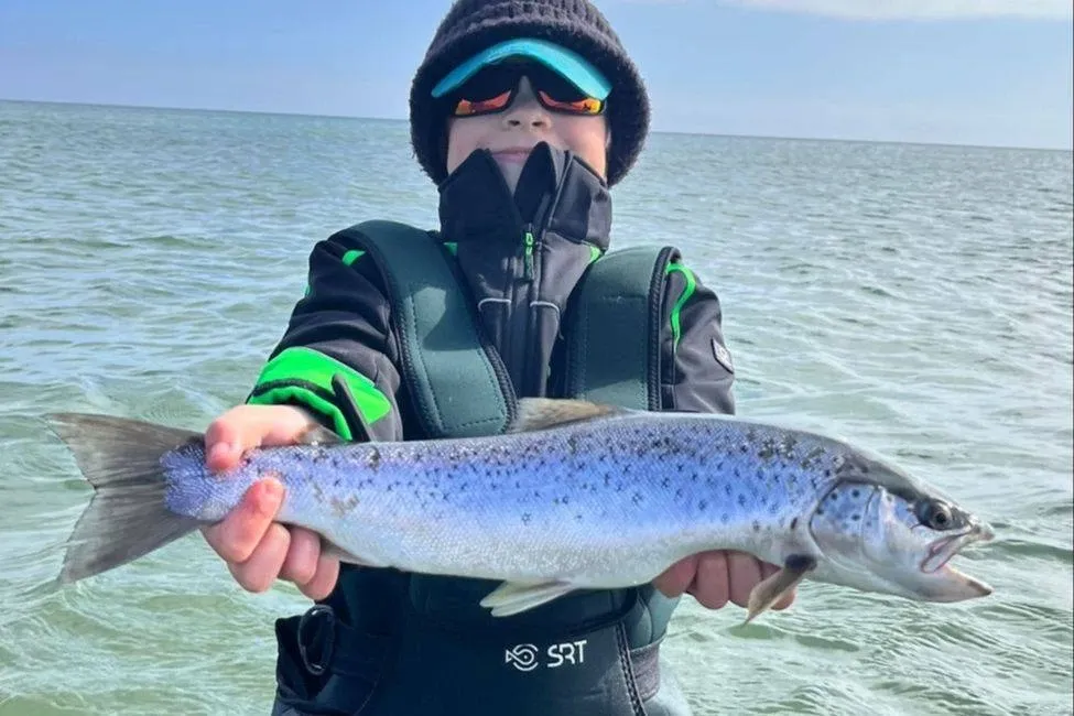 Junger Angler hält eine silberne Meerforelle in die Kamera